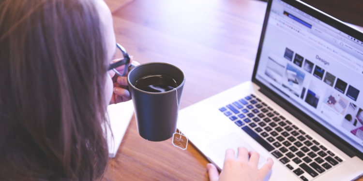 Photo of woman with cup of tea looking at laptop