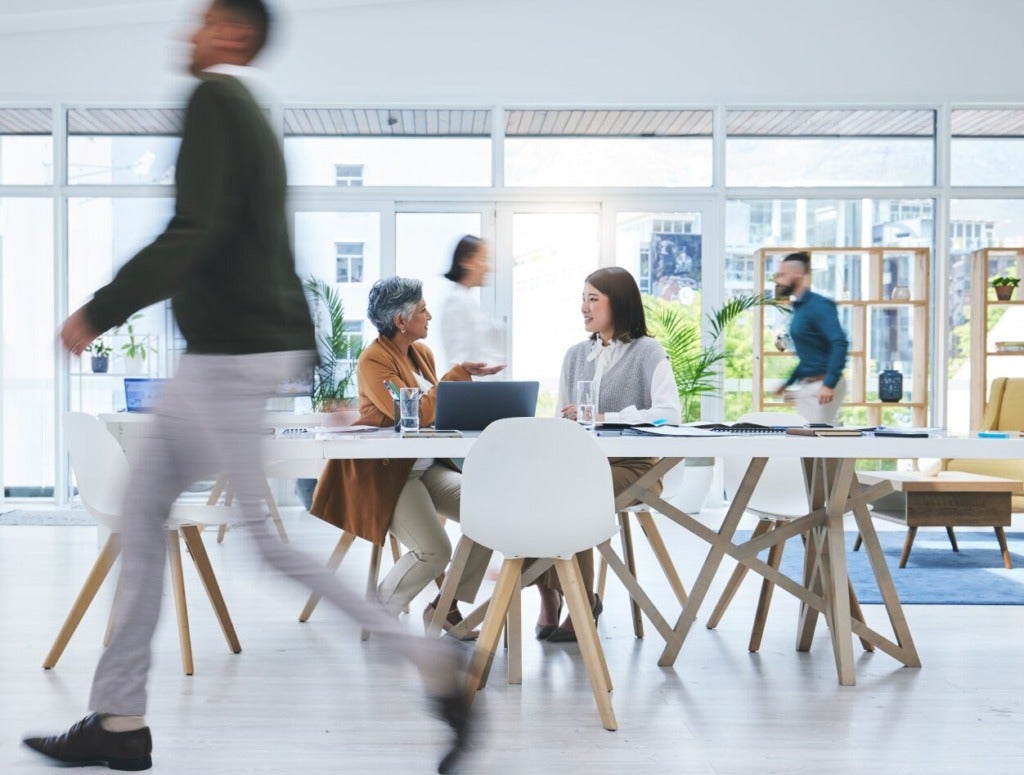 People at a conference table in a busy office environment.