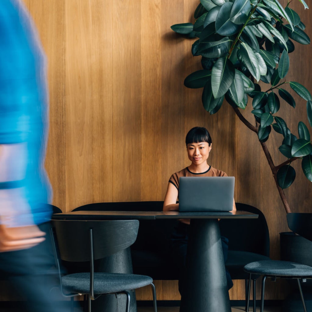 New hire sitting at a laptop in a stylish, modern office lounge, independently navigating onboarding materials or training content.