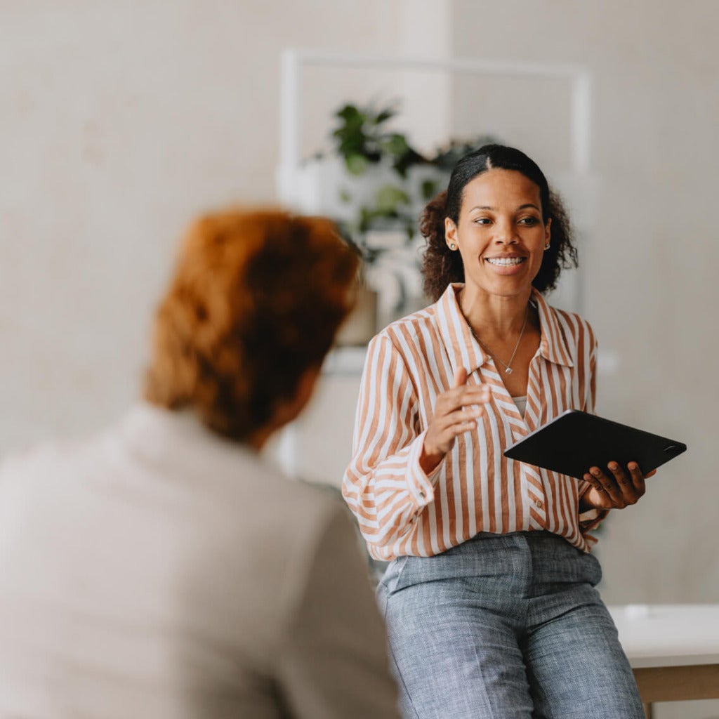 Smiling employee leading an onboarding session while holding a tablet, engaging in conversation with a colleague in a welcoming office setting.
