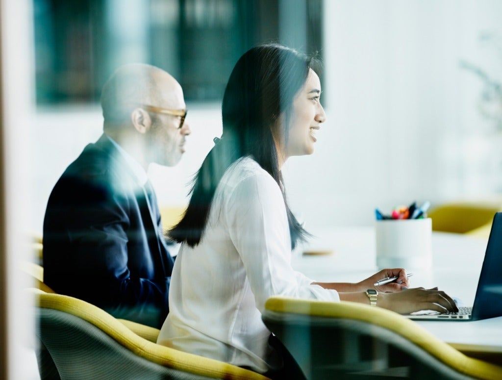 A man and woman at work in a glass conference room.